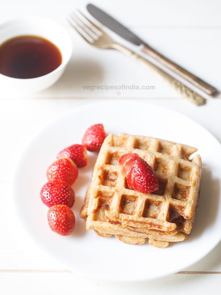 Breakfast waffles with strawberry slices on white plate.