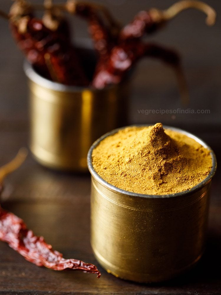 rasam powder in a brass container with container of dried red chilies in the back. 