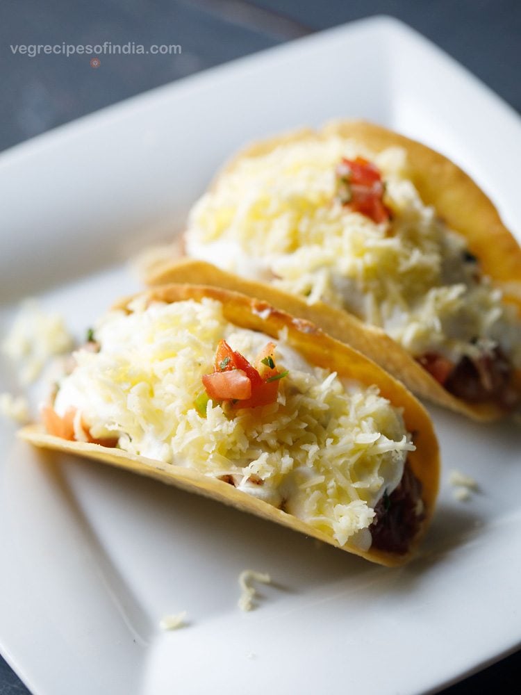 two Mexican veggie tacos on a white plate garnished with a bit of pico de gallo. 