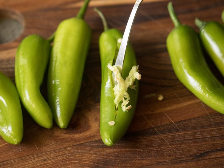 removing the seeds and pitch of a green chili with a spoon. 