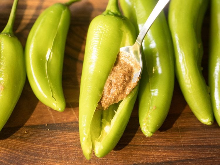 stuffing the prepared spice paste in a green chili with a spoon. 