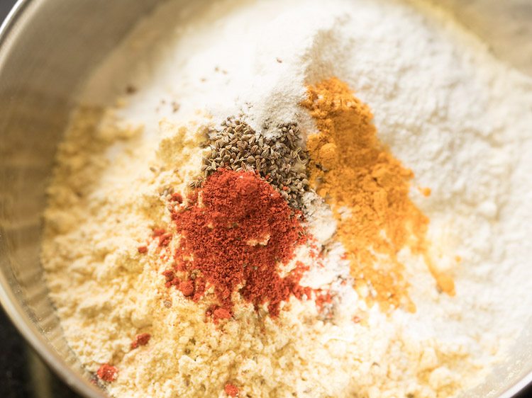 red chili powder, turmeric powder, asafoetida, caron seeds, baking soda and salt added to the gram flour-rice flour mixture. 