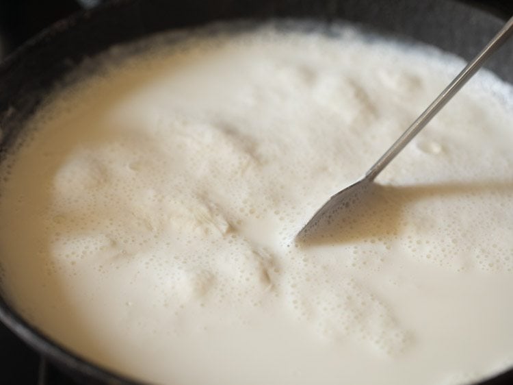 stirring and simmering milk for mishti doi recipe. 