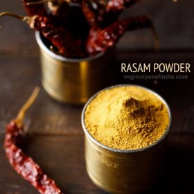 rasam powder in a brass container with container of dried red chilies in the back and text layover.