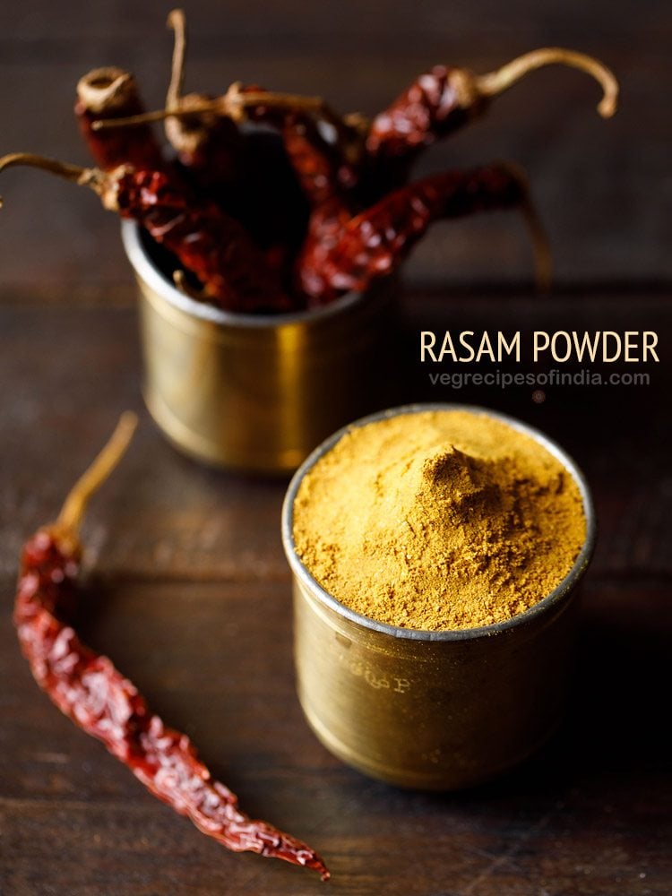 rasam powder in a brass container with container of dried red chilies in the back and text layover.