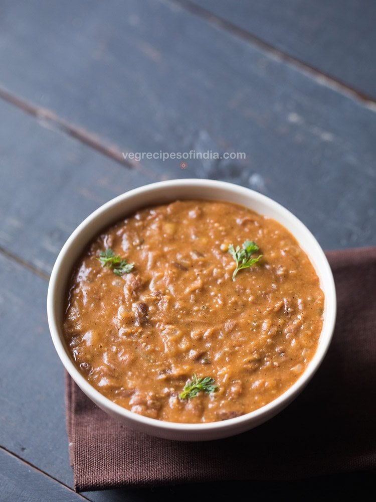 refried beans garnished with coriander leaves and served in a white bowl. 