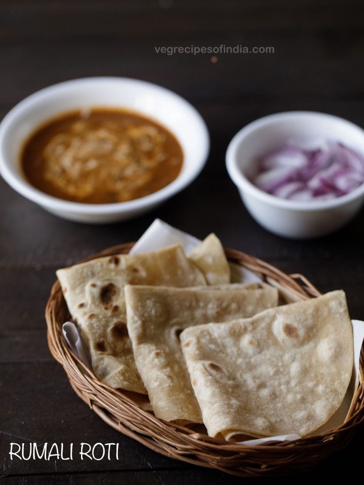 rumali roti folded and served in a basket with a bowl of curry and a bowl of onions kept in the background and text layover. 