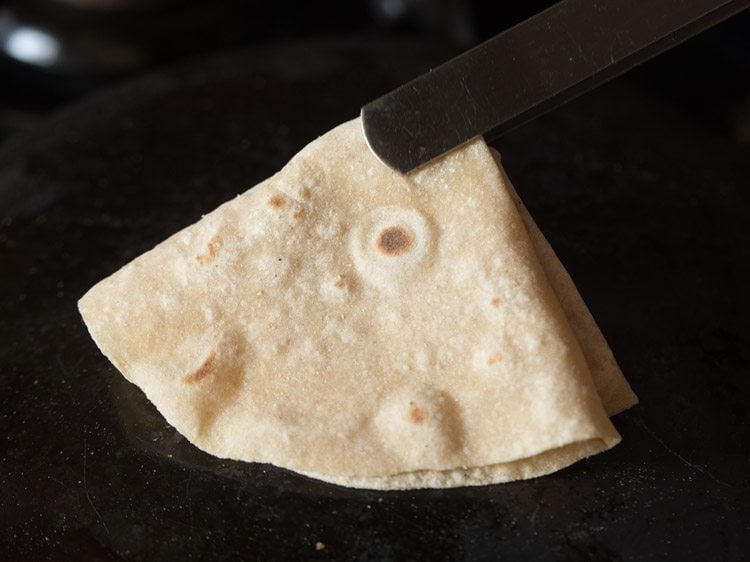 folding rumali roti with a tong. 