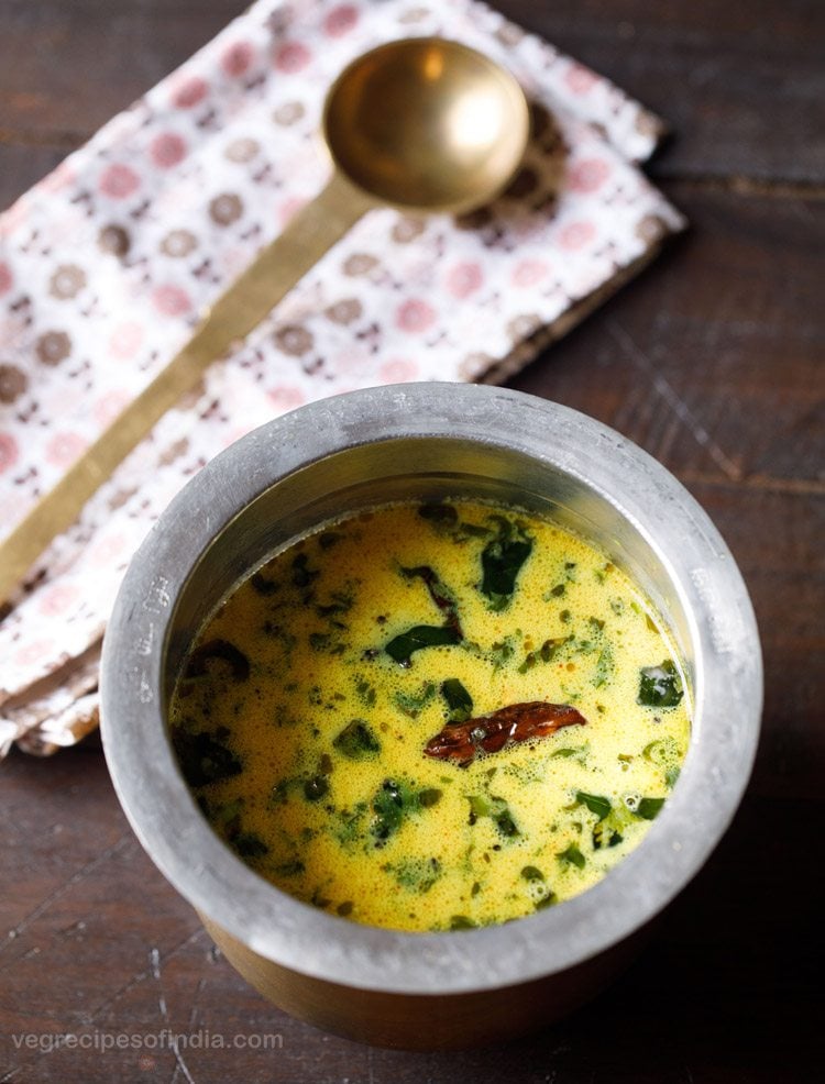 thengai paal rasam served in a brass pot with a spoon kept on the side. 