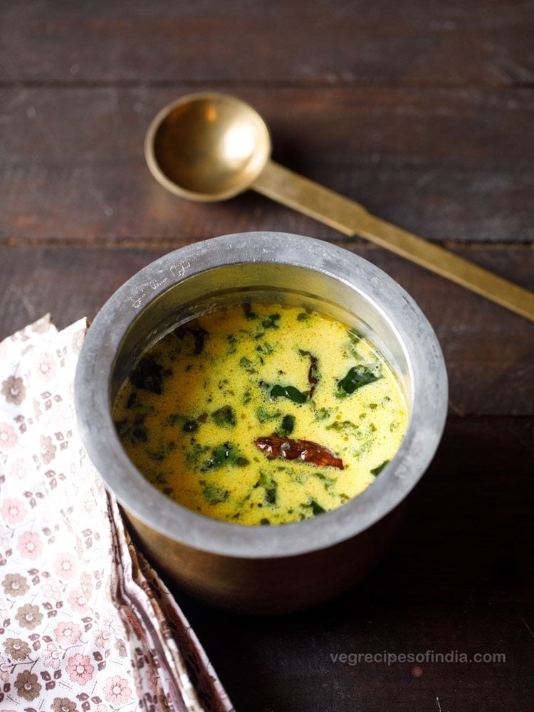 thengai paal rasam served in a brass pot with a spoon kept on the side. 