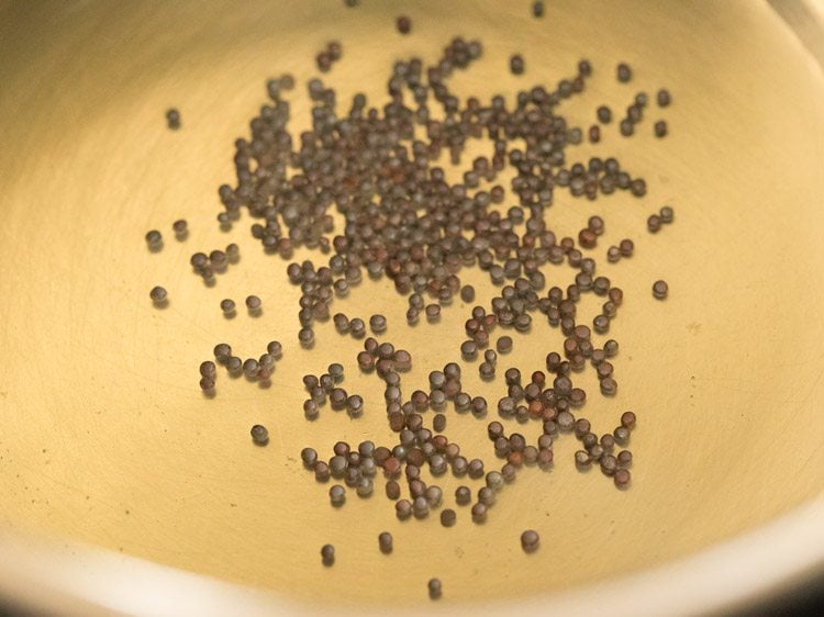 mustard seeds added to hot sesame oil in pan for vatha kuzhambu. 