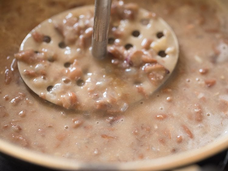 using a potato masher to mash refried beans. 