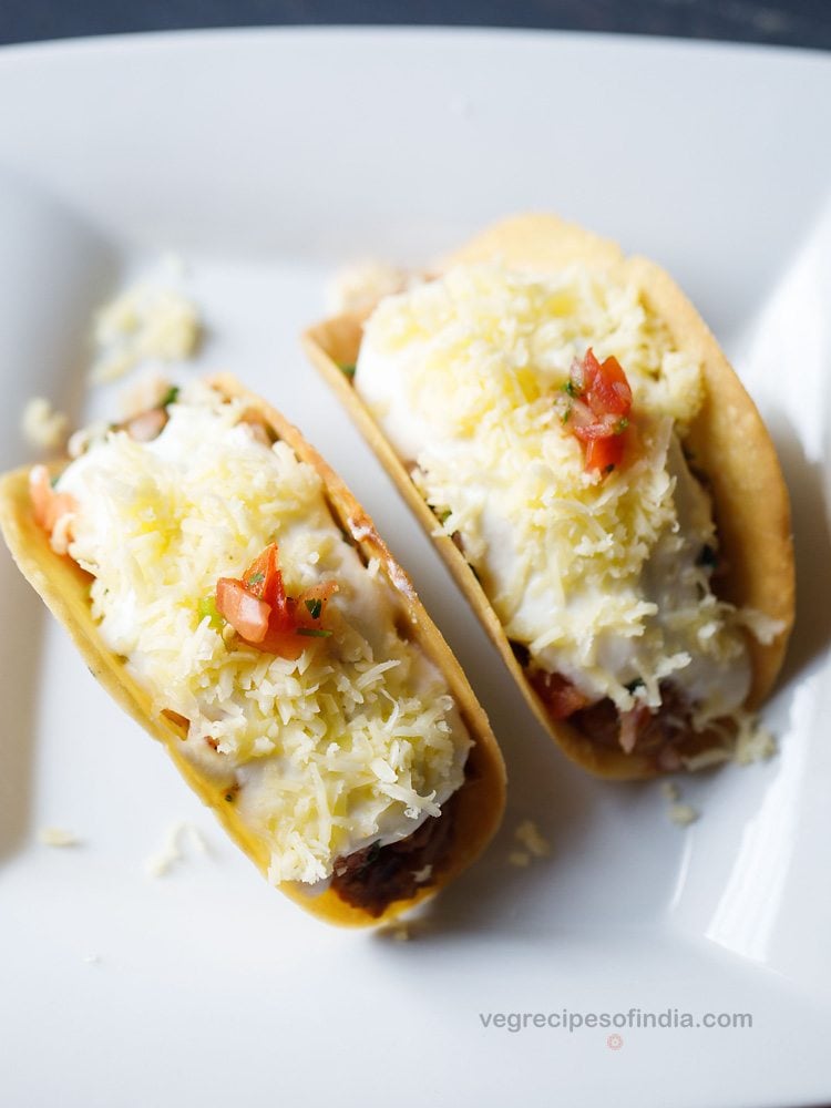 two veg tacos with refried beans on a square white plate. 