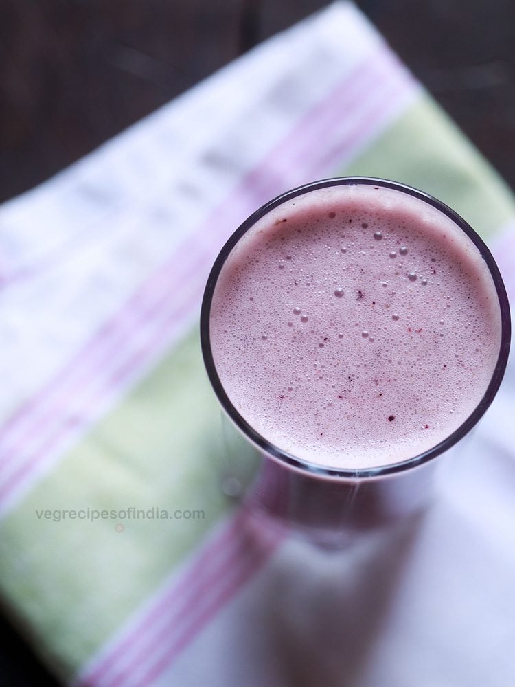 overhead shot of vegan blueberry smoothie in a glass placed on a white, pink and green cotton napkin