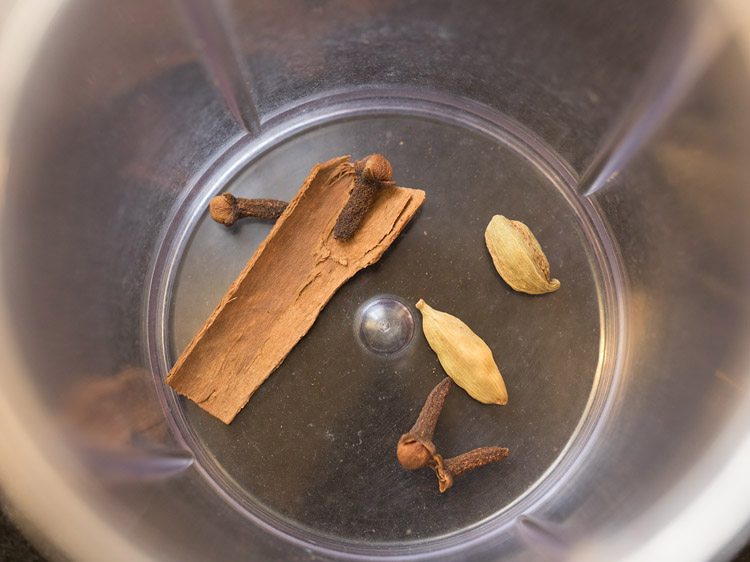 green cardamoms, cinnamon and cloves added to a grinder jar. 