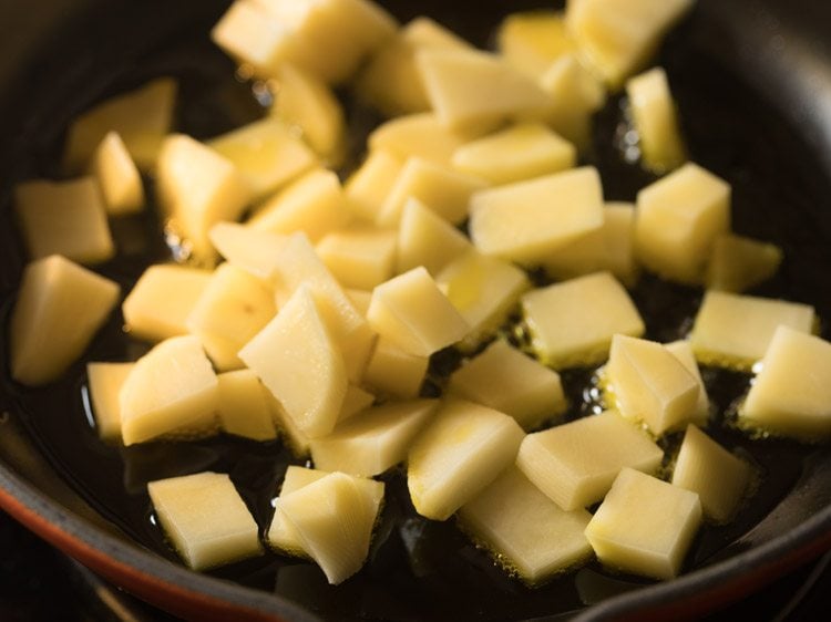 potato cubes added to hot mustard oil in pan. 