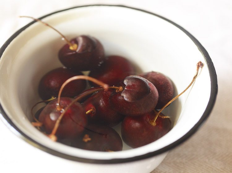 cherries soaked in water in a black rimmed white bowl.