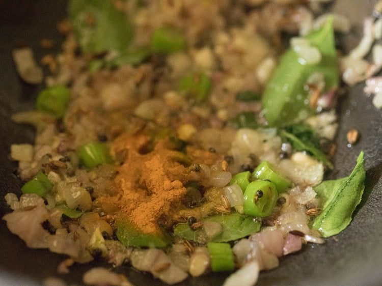 turmeric powder added to onion mixture in pan. 