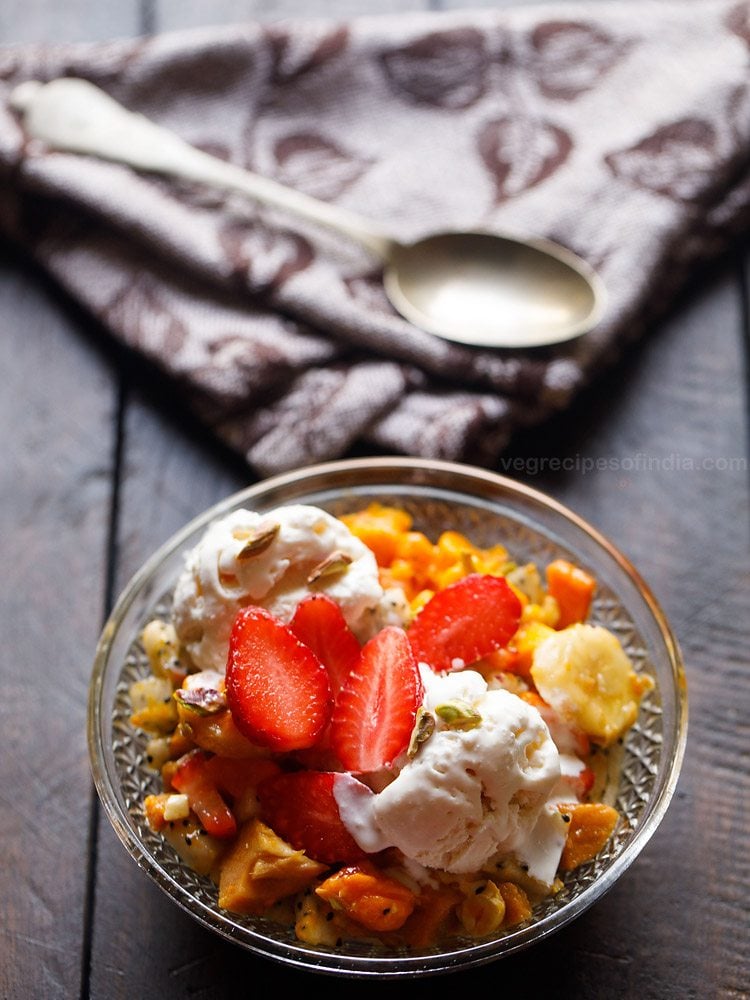 fruit salad with ice cream and nuts served in a glass bowl. 