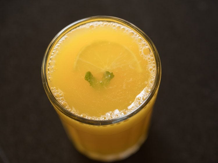 garnishing the fruit punch mocktail with fresh sliced fruit and a sprig of mint. 