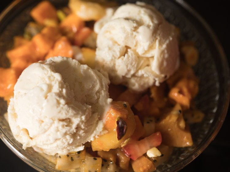 fruit salad topped with scoops of vanilla ice cream. 