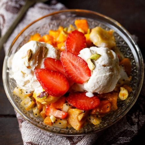 fruit salad with ice cream and nuts served in a glass bowl.