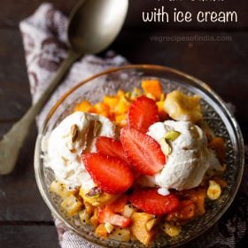 fruit salad with ice cream and nuts served in a glass bowl.