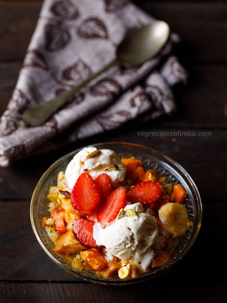 fruit salad with ice cream and nuts served in a glass bowl. 