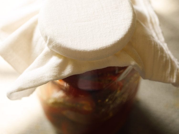 covering the mouth of the jar with a muslin cloth and securing it with a rubber band 