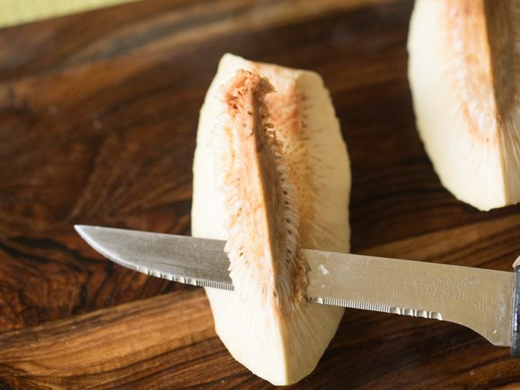 slicing off top spongy part of breadfruit halve. 