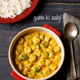 gatte ki sabji garnished with coriander leaves and served in a red casserole with a spoon kept on the right side and a bowl of steamed rice kept on the top left side and text layovers.