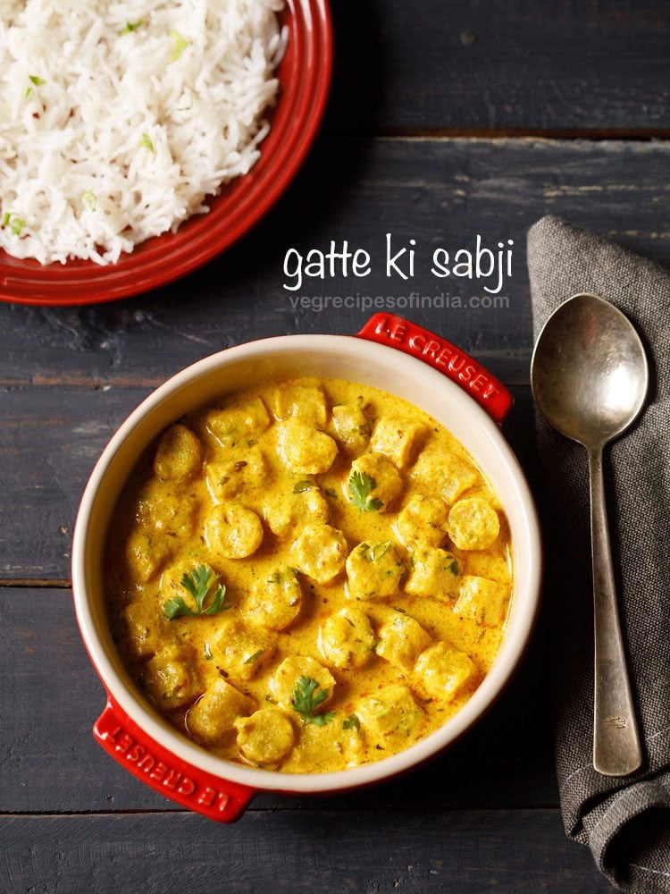 gatte ki sabji garnished with coriander leaves and served in a red casserole with a spoon kept on the right side and a bowl of steamed rice kept on the top left side and text layovers.