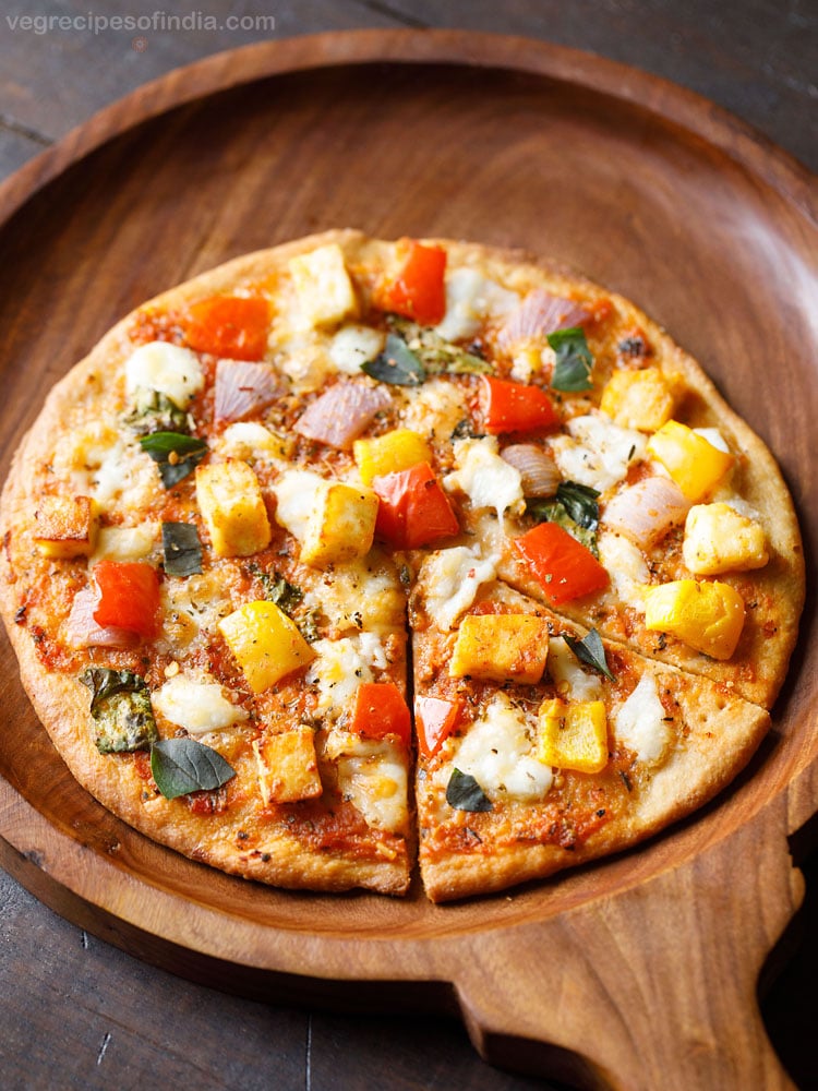 paneer pizza cut into a wedges and served on a wooden board.  