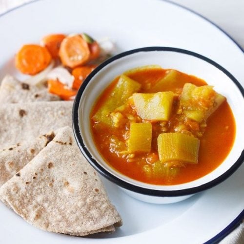 lauki ki sabji served in a blue rimmed bowl kept on a blue rimmed plate with chapattis kept on it on the left side and salad kept on a the left side on top.