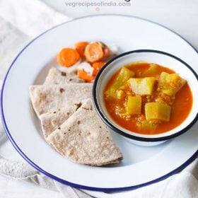 lauki ki sabji served in a blue rimmed bowl kept on a blue rimmed white plate with chapattis kept on the left side and salad kept on the top side on the plate with text layover.