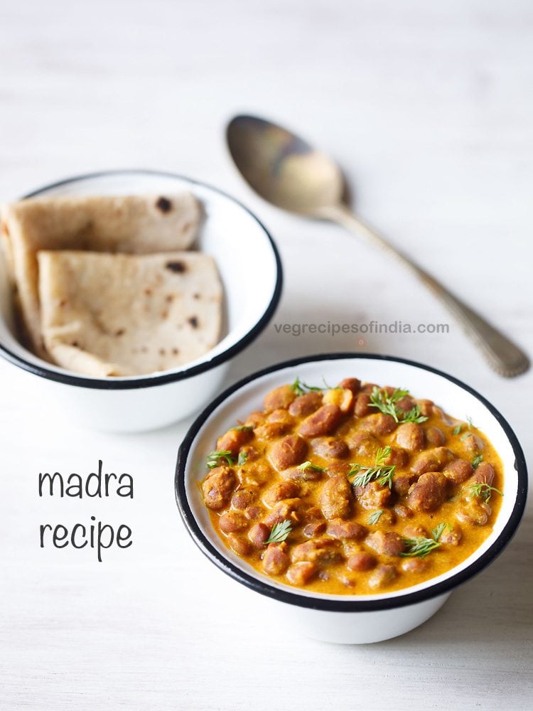 madra recipe garnished with coriander leaves and served in a black rimmed bowl with a bowl of chapatis and a spoon kept in the background and text layover.
