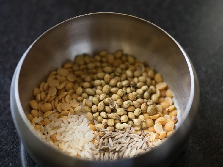 coriander seeds, tuvar dal, cumin seeds and raw rice added in a bowl for making paste for mor kuzhambu. 