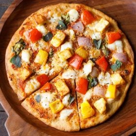 paneer pizza served on a wooden pizza board.