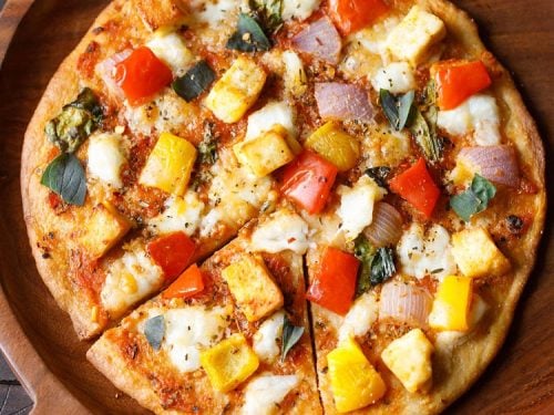 paneer pizza served on a wooden pizza board.
