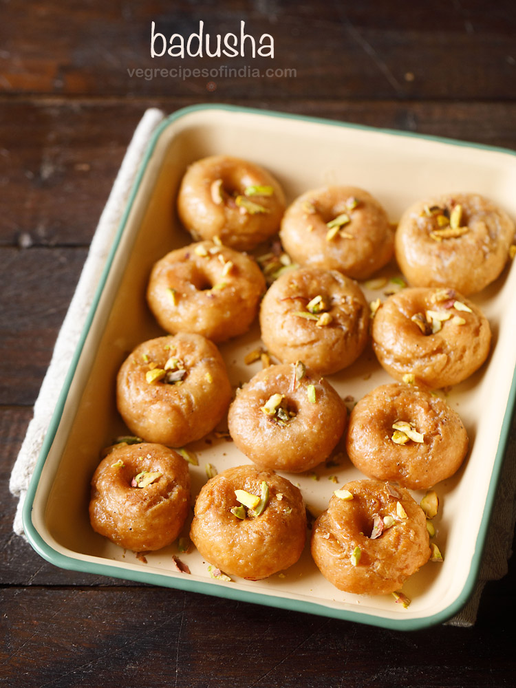 balushahi garnished with chopped pistachios and served in a ceramic tray with text layovers. 