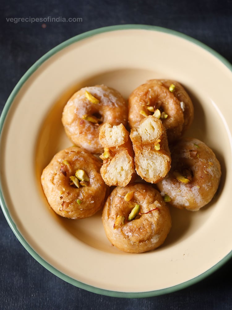 balushahi garnished with chopped pistachios and served in a ceramic plate with text layover. 