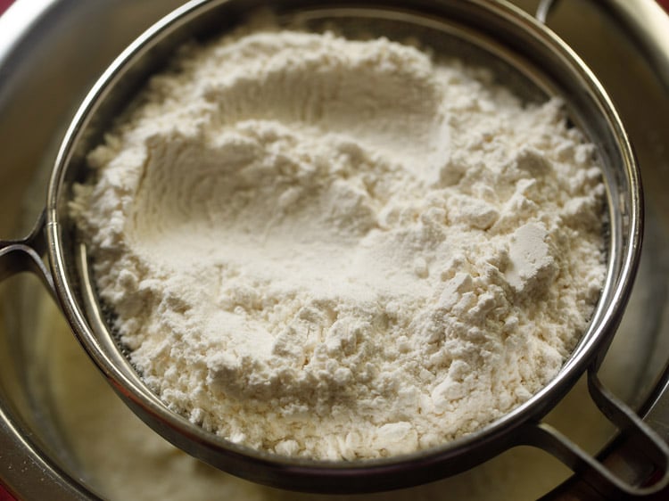 all purpose flour added in a sieve kept over the bowl for making badusha. 