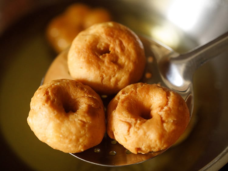 removing fried balushahi recipe from hot oil with a slotted spoon. 