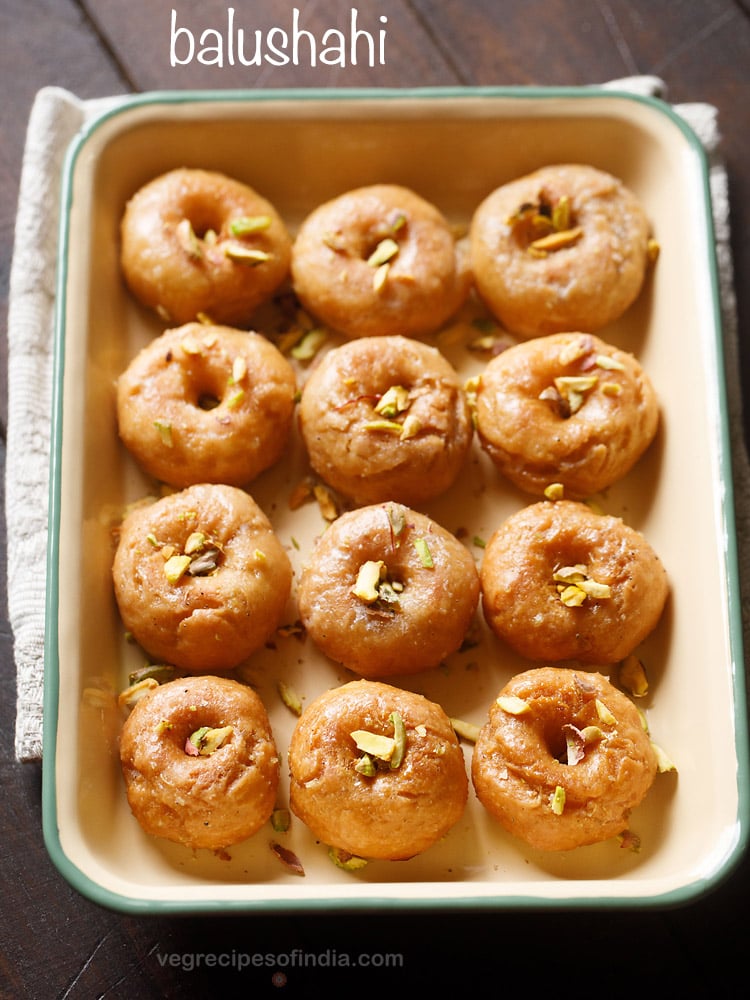 balushahi garnished with chopped pistachios and served in a ceramic tray with text layovers.