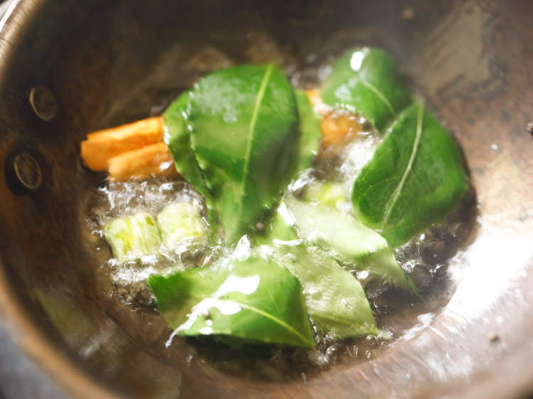 frying dried red chili, chopped green chilies and curry leaves in hot oil for tempering kappa puzhukku. 