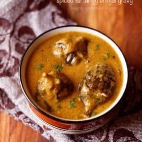 ennai kathirikai kulambu garnished with chopped coriander leaves and served in a black rimmed bowl with text layovers.