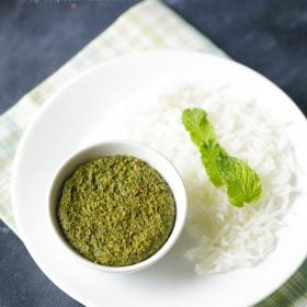 pudina thogayal served in a white bowl placed on white plate with steamed rice garnished with mint leaves and text layover.