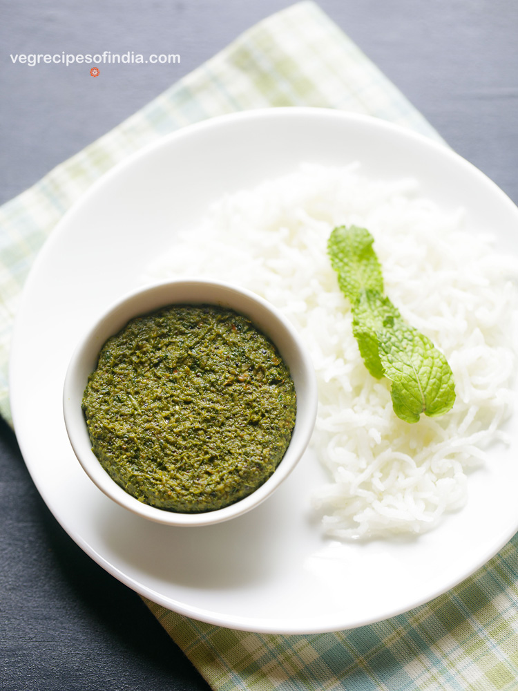 pudina thogayal served in a white bowl placed on white plate with steamed rice garnished with mint leaves and text layover. 
