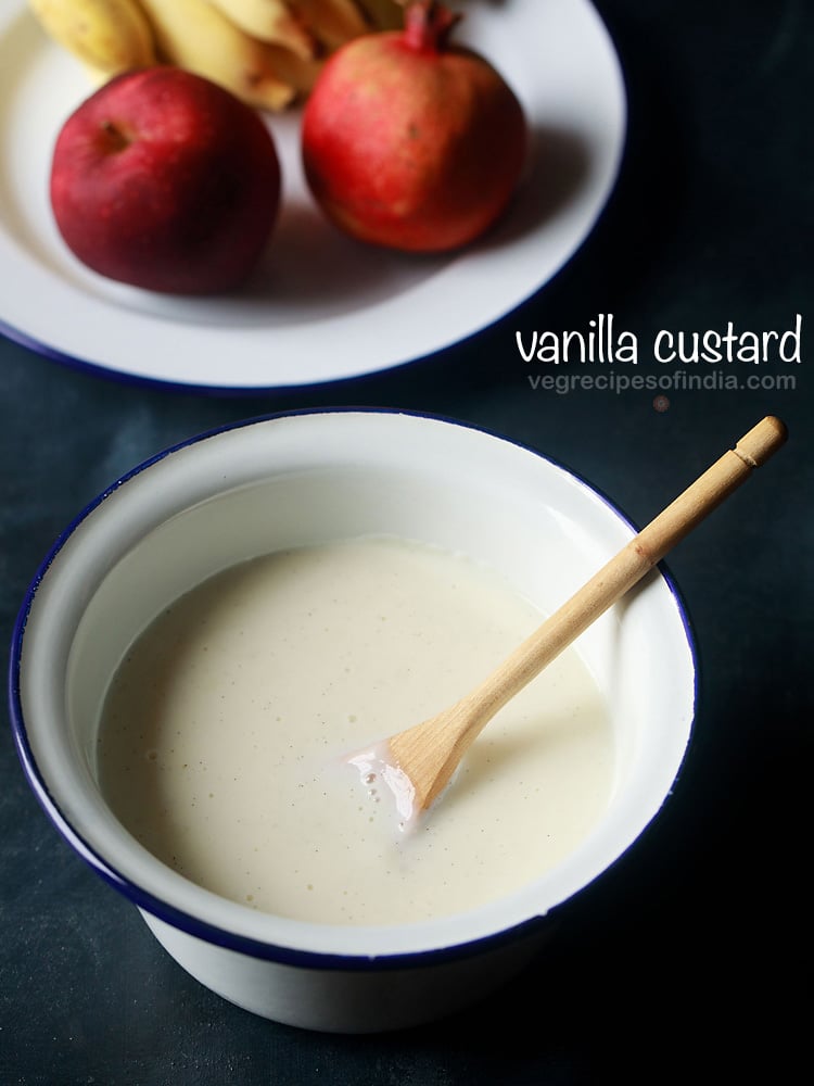 vanilla custard sauce in a bowl with a wooden spoon next to a plate of fresh fruit.