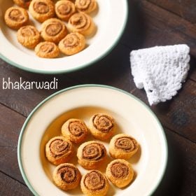 bhakarwadi pinwheels served in a green rimmed ceramic bowl with text layovers.